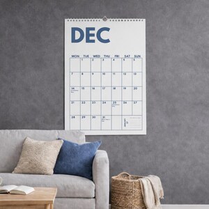 Pu&ograve; includere: Un calendario da parete per il mese di dicembre con sfondo bianco, testo blu scuro e rilegatura a spirale nella parte superiore. La griglia mostra i giorni della settimana da luned&igrave; a domenica, con date numerate e un piccolo calendario di gennaio.