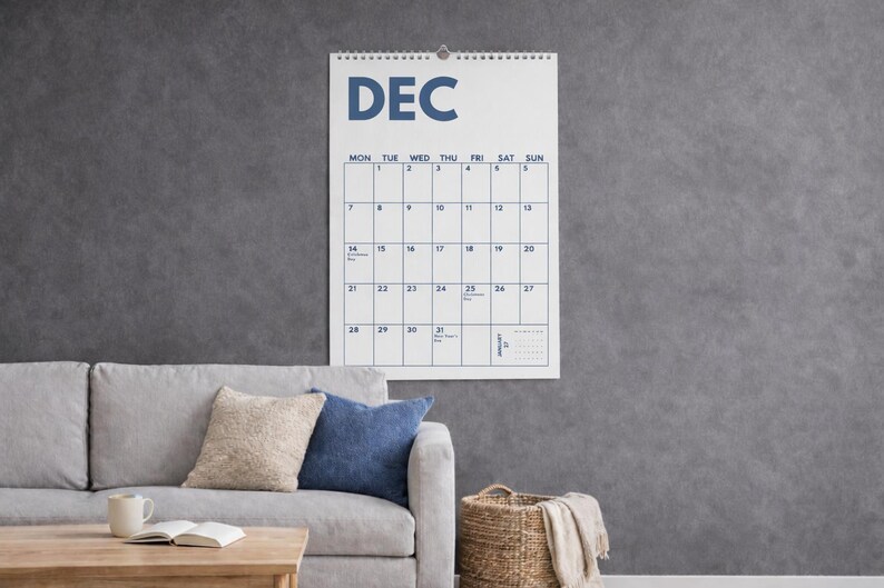 Pu&ograve; includere: Un calendario da parete per il mese di dicembre con sfondo bianco, testo blu scuro e rilegatura a spirale nella parte superiore. La griglia mostra i giorni della settimana da luned&igrave; a domenica, con date numerate e un piccolo calendario di gennaio.