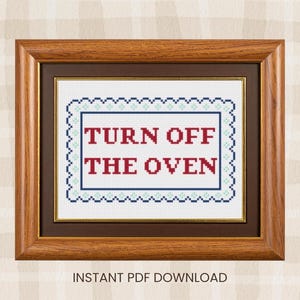 May include: A framed cross-stitch with the words "TURN OFF THE OVEN" in red, framed by a blue border with a scalloped edge. The frame is a warm brown color, and the background is a light plaid pattern.