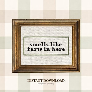 May include: A cross-stitch pattern framed in a metallic gold frame. The white fabric features a dark green border and the black text "smells like farts in here" in a pixelated font. The text "INSTANT DOWNLOAD" and "Keeepsake Kays on Etsy" appear below.