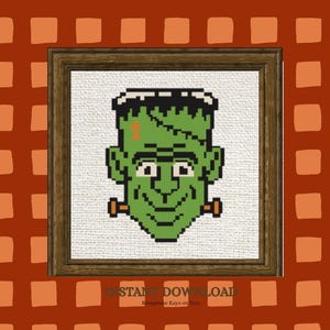 May include: A cross-stitch pattern featuring a pixelated green monster head with black hair, a stitched forehead scar, and orange neck bolts, framed in a dark wood border against a background of orange and dark red squares with text.