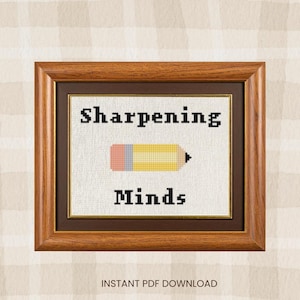 May include: A framed cross-stitch artwork with the words "Sharpening Minds" and a pencil graphic. The pencil is yellow, pink, and gray. The frame is brown with a dark brown matting. The background is a beige and white plaid pattern.