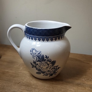 May include: White ceramic jug with a blue floral pattern and a blue patterned border. The jug has a curved handle and a spout. A classic piece for serving drinks, ideal for a kitchen or dining room.