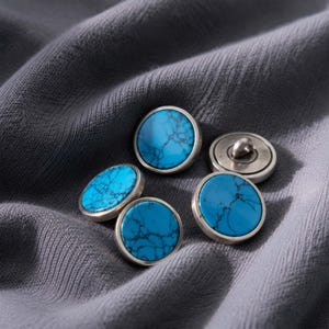 May include: Four round buttons featuring a bright blue surface with a dark, web-like veined pattern. Each button is encased in a smooth, metallic silver-toned rim. One button is positioned to show the metal loop shank on its underside.