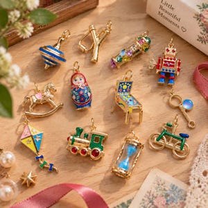 May include: A collection of gold-tone metal charms featuring various toy designs including a blue spinning top, a slingshot, a kaleidoscope, a robot, a rocking horse, a matryoshka doll, a pinball machine, a kite, a train, an hourglass, and a bicycle.