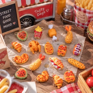 May include: A collection of miniature food-themed charms including a watermelon slice, french fries, a chicken leg, a shrimp tempura, a croissant, a whole roasted chicken, a hot dog, a pastry, and various other baked goods with metal loops.