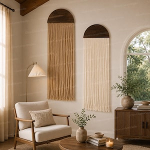May include: Two wall hangings featuring dark brown semi-circular wooden tops with long, vertical hanging cords. One wall hanging has tan cords, while the other has off-white cords. Both pieces are mounted on a wall, displaying a fringe design.