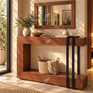 May include: A rectangular wooden console table with a dark wood grain finish and two vertical black metal supports on the right side. A woven basket with a light-colored cloth, a ceramic vase with greenery, a wooden bowl, and a mirror are included.