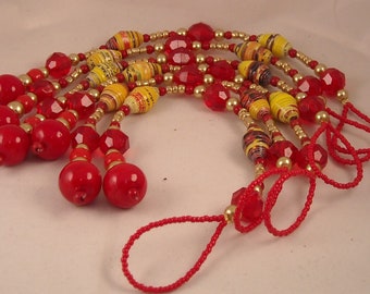 May include: A red and yellow beaded necklace with a tassel. The necklace is made with paper beads and red glass beads.