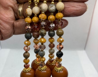 May include: Five brown beaded necklaces with gold accents. Each necklace features a large brown ball at the end. The beads are a mix of brown, gold, and clear.