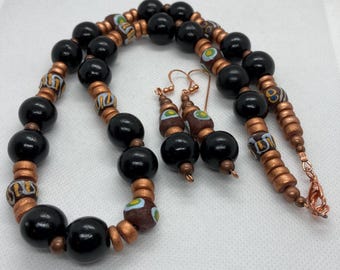 May include: A black and copper beaded necklace and matching earrings. The necklace features large black beads interspersed with smaller copper beads with colourful patterns. The earrings are made of black and copper beads with a copper wire hook.