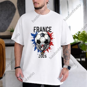 May include: White t-shirt featuring a soccer ball design with the word "FRANCE" above it. The design includes red, white, and blue accents, a skull, and the year "2026". The shirt is a casual, short-sleeved style.