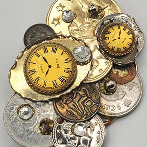 Peut inclure: Un assemblage unique de pièces de monnaie et de cadrans de montre. Les montres ont des cadrans jaunes avec des chiffres romains et le mot "Paris". Diverses pièces, dont une pièce d'or avec un aigle, sont ornées de strass et d'autres embellissements.