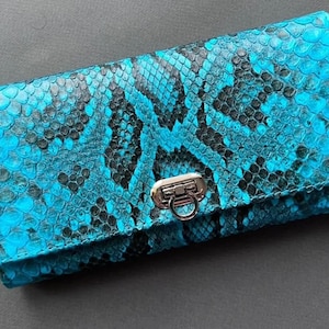 May include: A turquoise and black snakeskin-effect wallet with a silver clasp. The rectangular wallet is made of leather. The snakeskin pattern is detailed and covers the entire surface of the wallet.