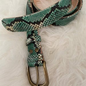 May include: A white ceramic mug with a black handle and the text "But First, Coffee" in a bold, black font. The mug is set against a blurred background, suggesting a cozy setting.