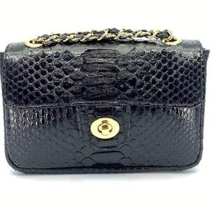 Puede incluir: Pequeño bolso negro con un patrón texturizado similar a la piel de serpiente. Cuenta con una correa de cadena dorada y un cierre dorado. El diseño es elegante y compacto, ideal para llevar lo esencial. Dimensiones compactas.