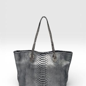 May include: A silver-toned tote bag with a snakeskin pattern. The bag has two handles and a rectangular shape. The snakeskin pattern is visible on the body and handles of the bag.