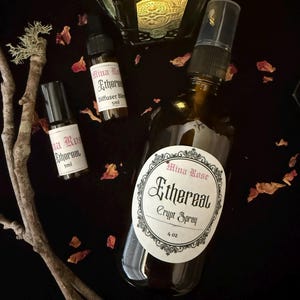 May include: A 4 oz amber glass spray bottle labeled Mina Rose Ethereal Crypt Spray, alongside two 5ml amber glass bottles labeled Mina Rose Ethereal Diffuser Blend, scattered with dried flower petals and a piece of lichen-covered wood.