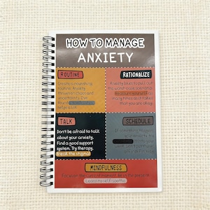 Könnte beinhalten: Ein spiralgebundenes Notizbuch mit dem Titel "HOW TO MANAGE ANXIETY". Die Seiten des Notizbuchs sind in Abschnitte unterteilt, die Ratschläge zur Bewältigung von Angstzuständen geben, darunter "ROUTINE", "RATIONALIZE", "TALK", "SCHEDULE" und "MINDFULNESS".