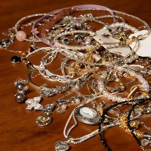 Op de afbeelding: Een verzameling diverse sieraden, waaronder kettingen, armbanden en oorbellen. Het assortiment bevat zilver- en goudtinten, parels en decoratieve hangers. Sommige items hebben edelstenen en ingewikkelde ontwerpen, wat een gevarieerde weergave van accessoires creëert.