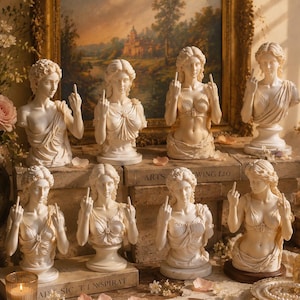May include: A collection of eight off-white classical-style female busts arranged on stacked books. Each figure is depicted with a draped garment and is shown making a middle finger gesture with one or both hands. The busts are set against a landscape painting.