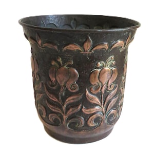 May include: A dark brown copper planter with an embossed floral design. The flowers are in a copper color.