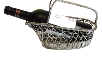 Puede incluir: Una cesta de vino de metal plateado con asa, que contiene una botella de vino oscuro y una etiqueta blanca. La cesta tiene un diseño tejido y está diseñada para contener una sola botella de vino.