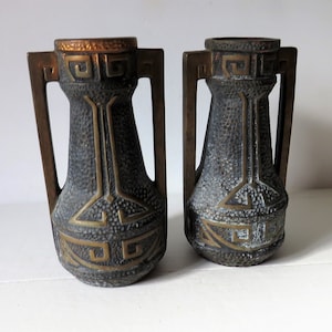 May include: Two decorative ceramic vases with gold accents and geometric patterns. The vases have a textured surface and are a dark brown color.