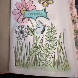 Puede incluir: Una p&aacute;gina de una Santa Biblia con una ilustraci&oacute;n dibujada a mano de una flor rosa con una pancarta verde azulado con la etiqueta HOLY BIBLE, un diente de le&oacute;n, follaje verde y dos mariposas, una amarilla y gris y la otra azul claro, coloreadas.