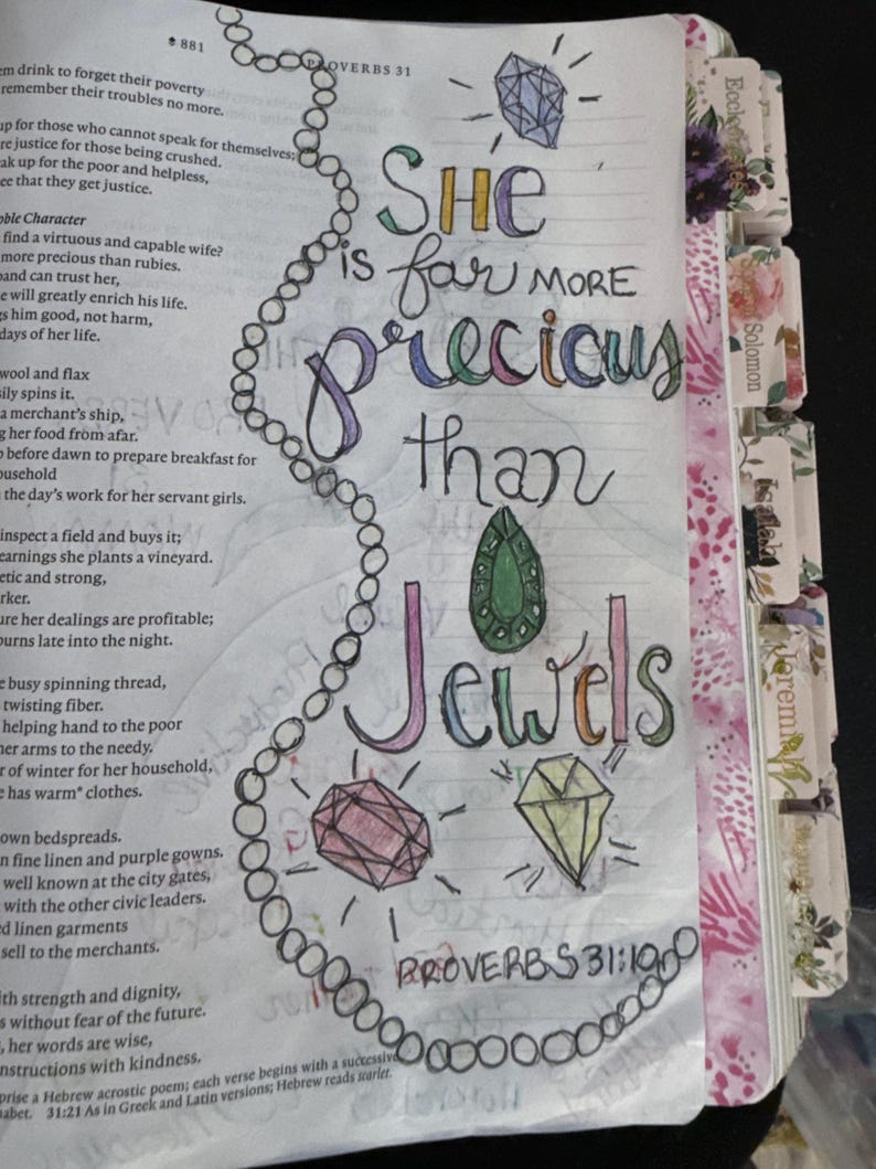 Puede incluir: Una p&aacute;gina de la Biblia con ilustraciones y caligraf&iacute;a hechas a mano. El texto dice, She is far more precious than Jewels, Proverbs 31:10. La p&aacute;gina incluye un collar de perlas dibujado, un diamante azul y gemas verde, rosa y amarilla.