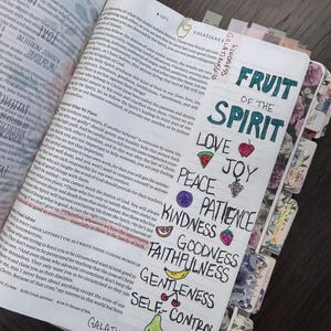 Puede incluir: Una p&aacute;gina de Biblia abierta que presenta una lista escrita a mano titulada Fruit of the Spirit. El texto incluye Love, Joy, Peace, Patience, Kindness, Goodness, Faithfulness, Gentleness y Self-Control, acompa&ntilde;ado de peque&ntilde;os dibujos de frutas a color.