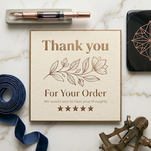 May include: A cream-colored card with the words "Thank you" and "For Your Order" in embossed brown lettering. A floral design and five stars are also featured. A rose gold fountain pen rests in a concrete pen holder.