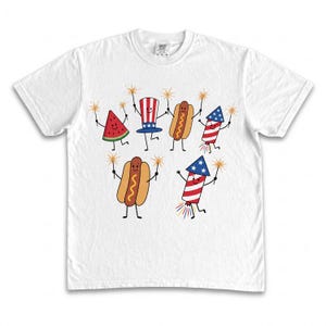 Pode incluir: Camiseta branca com um design divertido de melancia animada, cachorros-quentes e fogos de artifício, cada um segurando estrelinhas. Os personagens são adornados com cores e símbolos patrióticos, perfeitos para as celebrações do Dia da Independência.