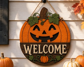 May include: A circular wooden door sign featuring a carved orange jack-o'-lantern with green leaves and a brown stem. The lower section is dark brown with the word WELCOME in light-colored lettering. A rope hanger is attached to the top.