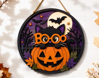 May include: A circular layered wooden wall hanging featuring a black cat wearing orange glasses with the text BOO, sitting inside a carved orange pumpkin. The background shows a purple sky, a full moon, black trees, bats, and orange stars.