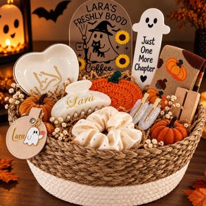 May include: A woven basket filled with Halloween-themed items including a heart-shaped dish, a ghost-shaped bookmark with the text Just One More Chapter, a crochet pumpkin, a hair claw with the name Lara, a scrunchie, and a keychain with a ghost.