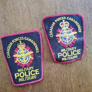 May include: Two black embroidered patches with red borders featuring the text Canadian Forces Canadiennes and Military Police Militaire. The center displays a gold emblem with a crown, wings, and anchor surrounded by red maple leaves on a black field.