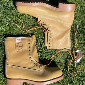 Könnte beinhalten: Ein Paar hellbraune Leder-Arbeitsstiefel mit braunen Sohlen und Schnürsenkeln. Die Stiefel haben ein hohes Design mit mehreren Ösen für die Schnürsenkel. Der Text "TUF MAC 891 INSULATED" ist auf der Seite zu sehen.