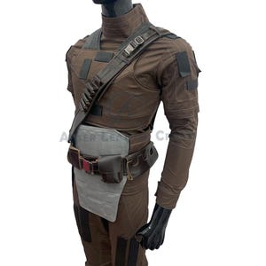 May include: A brown tactical costume with a shoulder strap, belt, and pouches. The outfit features a high collar, multiple pockets, and a grey protective panel. The mannequin is on a white background.