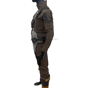May include: A brown costume with a high collar, shoulder pads, and multiple pockets. The outfit includes a belt with pouches, gloves, and boots. The costume has a futuristic or military design.