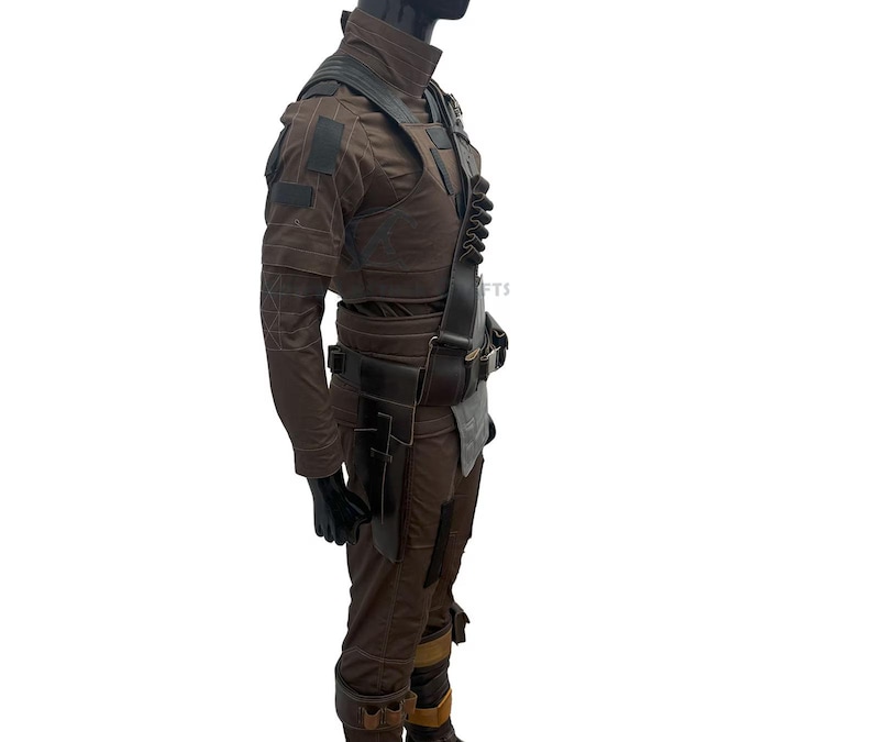 May include: A brown costume comprising a jacket, trousers, and a utility belt. The jacket features multiple pockets and patches. The trousers have knee pads, and the belt has pouches. The costume is displayed on a mannequin.
