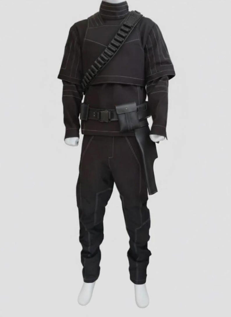May include: A black costume with white stitching, featuring a high-collared top, long sleeves, and matching pants. The outfit includes a belt with a pouch, a shoulder strap, and a holster-like piece. The costume is displayed on a mannequin.