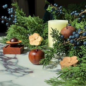 May include: A collection of small wooden objects including a dark brown sphere on a square base, a smooth wooden apple topped with a light-coloured carved flower, a second dark wooden apple, and a separate carved wooden flower piece.
