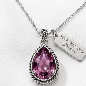 Puede incluir: Collar plateado con un colgante grande en forma de l&aacute;grima. El colgante presenta una piedra preciosa facetada de color rosa intenso, enmarcada por un dise&ntilde;o de cuerda trenzada. Una peque&ntilde;a etiqueta con el texto "YOUR TRUE COLOR Brighton" est&aacute; unida a la cadena.