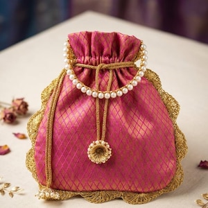 May include: A fuchsia drawstring pouch featuring a gold diamond-patterned weave, a scalloped gold lace trim along the edges, and a handle made of white pearls. The bag includes a gold drawstring cord finished with a decorative pearl-accented tassel.