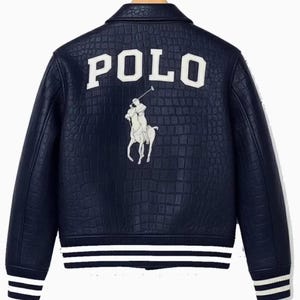 Può includere: Giacca in pelle blu navy con effetto coccodrillo. La parte posteriore presenta la scritta "POLO" in lettere bianche sopra un logo di giocatore di polo bianco. Strisce bianche adornano i polsini e l'orlo.