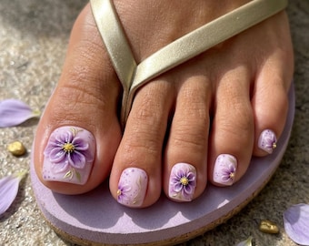 Puede incluir: Un par de chanclas de color morado claro con una tira dorada. Las uñas de los pies están pintadas de un suave lavanda con arte floral morado en relieve, con centros amarillos y delicados detalles de pan de oro en cada uña.