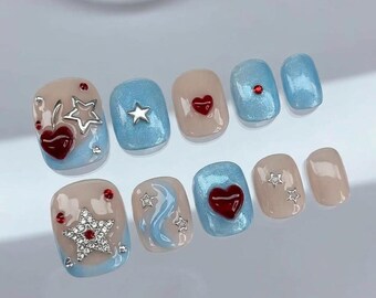 Puede incluir: Un juego de diez uñas postizas con una base que alterna tonos nude y azul claro brillante. Los diseños incluyen corazones rojos en relieve, adornos plateados en forma de estrella, pequeños brillantes rojos y detalles de ondas azules.