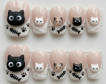 Puede incluir: Un juego de diez uñas postizas con base color nude y puntas blancas. Cada uña está decorada con una cara de gato en relieve 3D, huellas de patas negras y espinas de pescado negras. Las caras de los gatos son negras, blancas o tricolores.