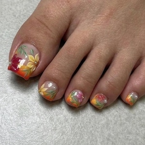 May include: A close-up of a foot with painted toenails. The nails feature a floral design with yellow, red, and orange gradients. Some nails have small pearl accents. The design includes leaves and flowers.
